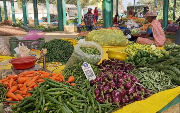 This image shows a vegetable market stall with a variety of fresh produce displayed on a cloth. A QR code for digital payment leans against a bag of beans.